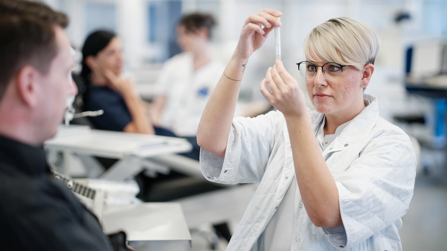 Sygeplejerske gør kanyle klar mens patient venter ved siden af.